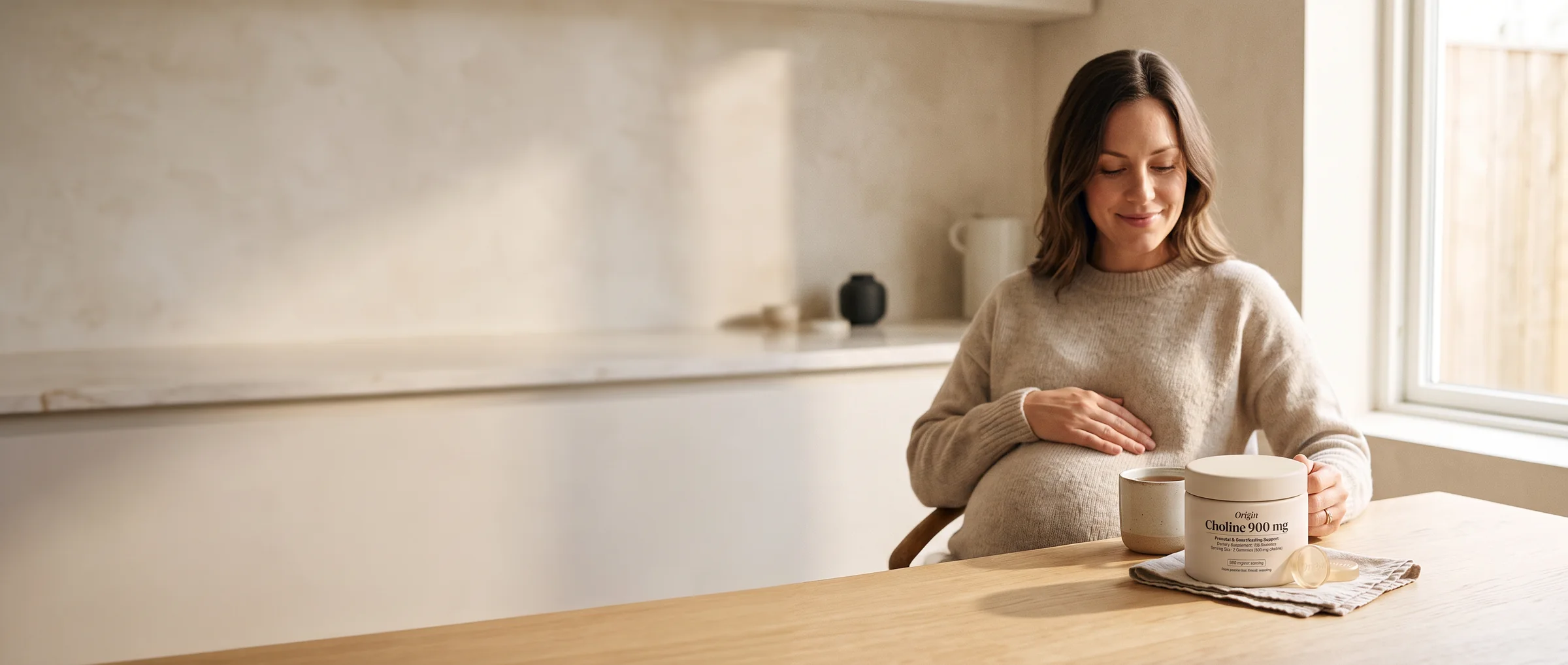 A pregnant woman at a sunlit kitchen table with a jar of Origin Prenatal Choline gummies